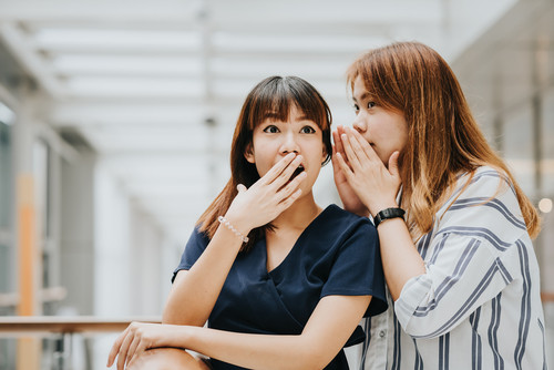 韓国出身のアジア人女性 2 人が口を覆いながら話している。