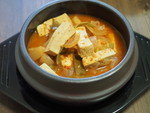 テーブルの上の黒い器に豆腐が盛られ、味噌だれがかかっています。