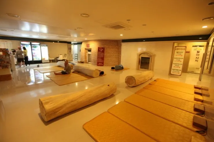 韓国の伝統的なサウナの広い部屋で、床にたくさんのマットが敷かれています。