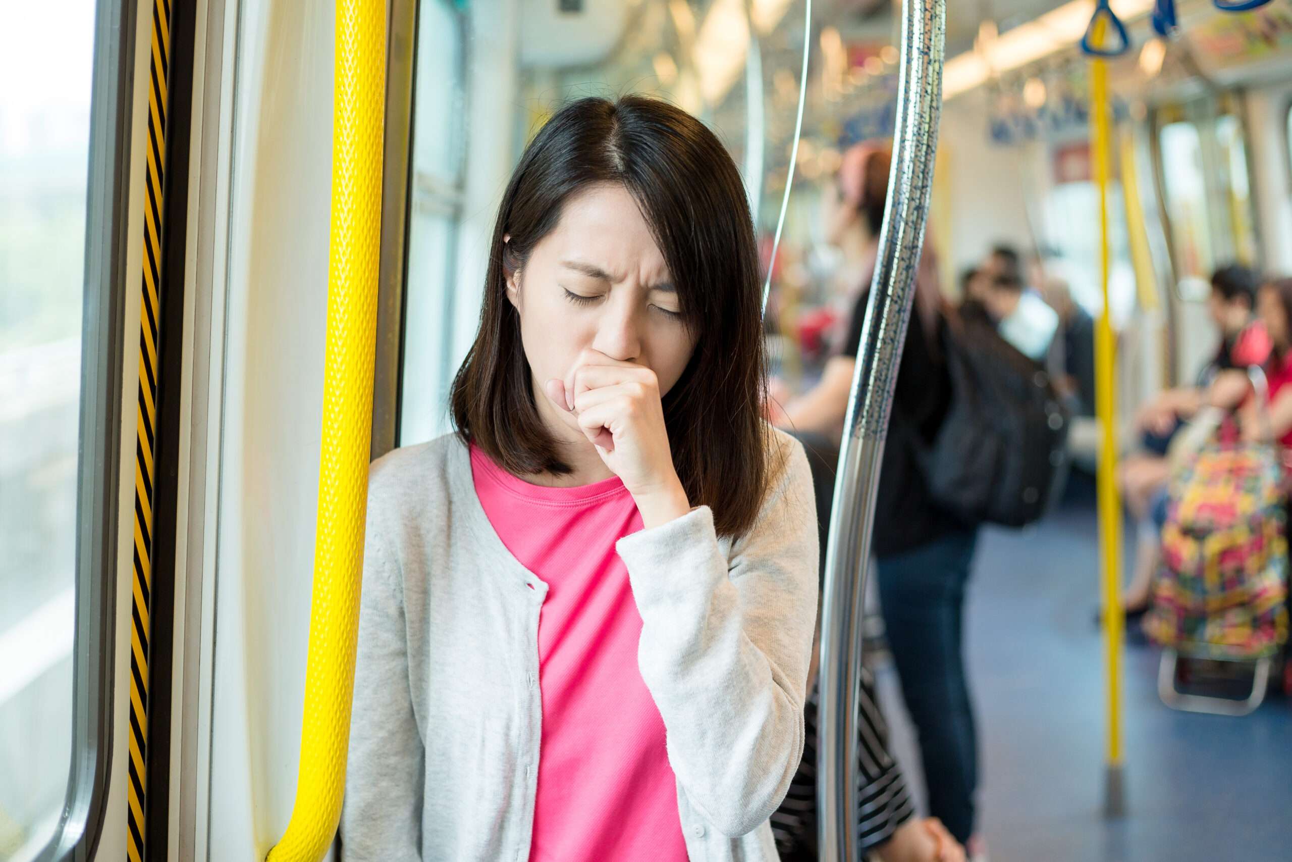 電車内で女性がくしゃみをしており、近くにいた他の乗客に誤って細菌をまき散らしている。