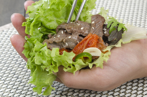 肉が入った韓国のレタス包みを持つ人の手。