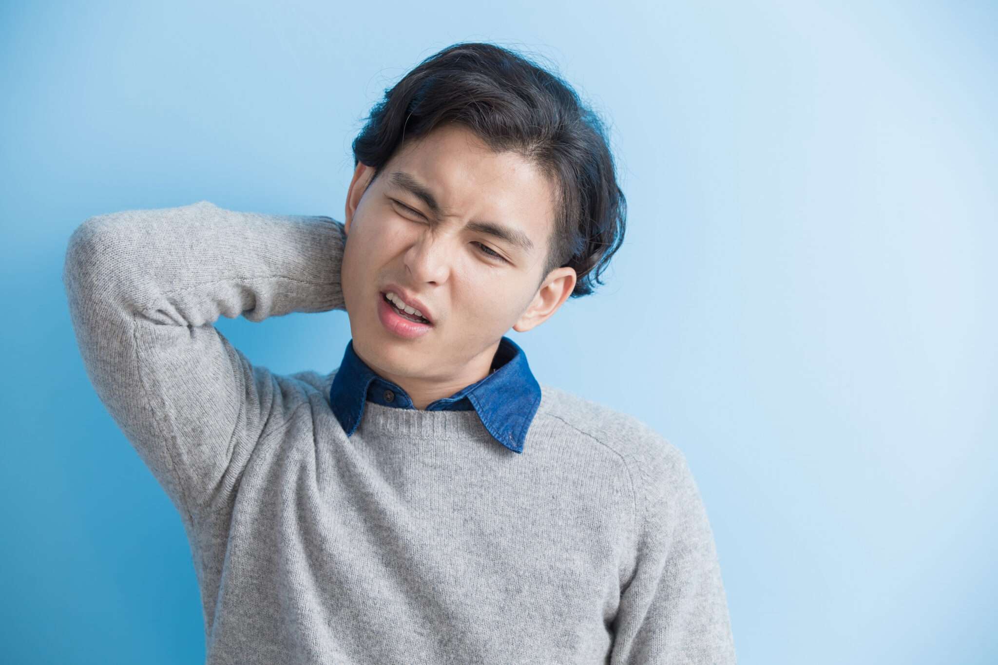 韓国の青い背景に首の痛みを持つ若い男性。