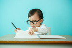眼鏡をかけた赤ちゃんが机に座って書き物をしており、愛らしい学力の可能性を示しています。