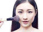 女性がブラシを使って顔に化粧をしています。