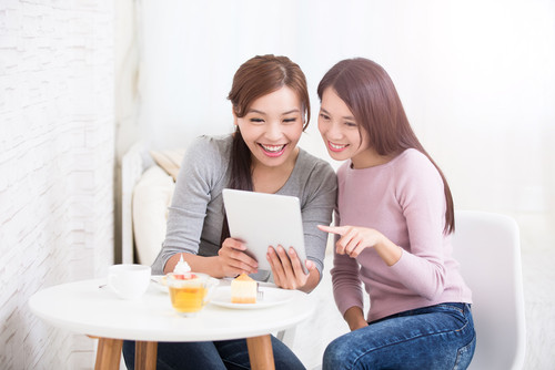 韓国から来た 2 人のアジア人女性がテーブルに座ってタブレット コンピューターを見ています。