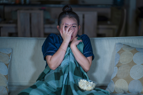 ポップコーンを膝に乗せてソファに座り、韓国映画マラソンを楽しむ女性。