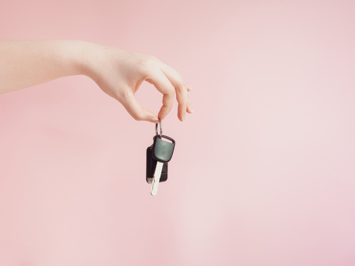 韓国のピンクの背景に車のキーを持つ女性の手。