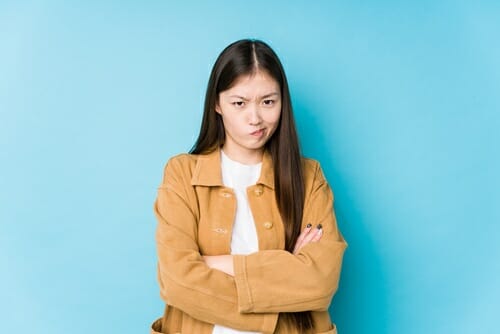青い背景に腕を組み、自信に満ちた姿勢を示すアジア系の若い女性。