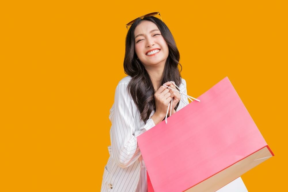 韓国のオレンジ色の背景に買い物袋を持つアジアの女性。