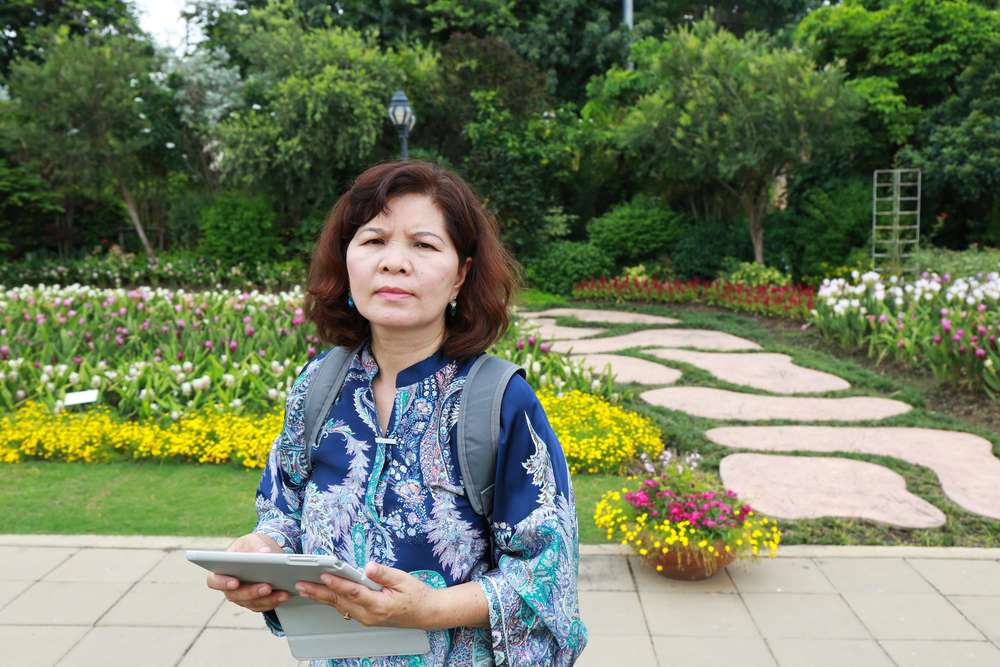 鮮やかな花と静かな石畳が敷かれた美しい韓国庭園の前に、石板を持った女性が立っています。