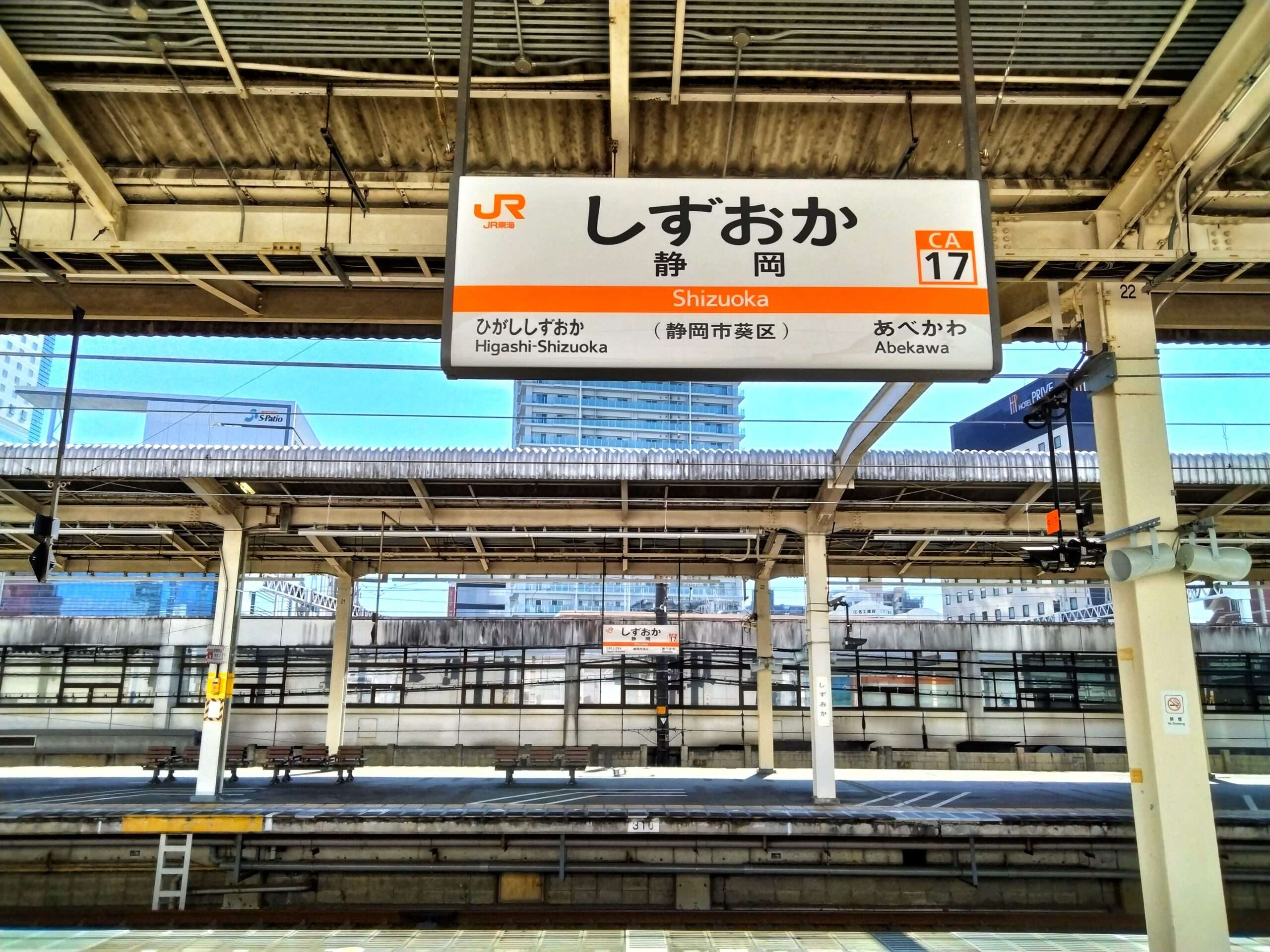静岡・三島の活気ある文化に囲まれた静岡駅の空いているホームには、目立つ駅名標が掲げられています。建物が都会的な背景を演出し、地域の賑やかな生活を反映しています。