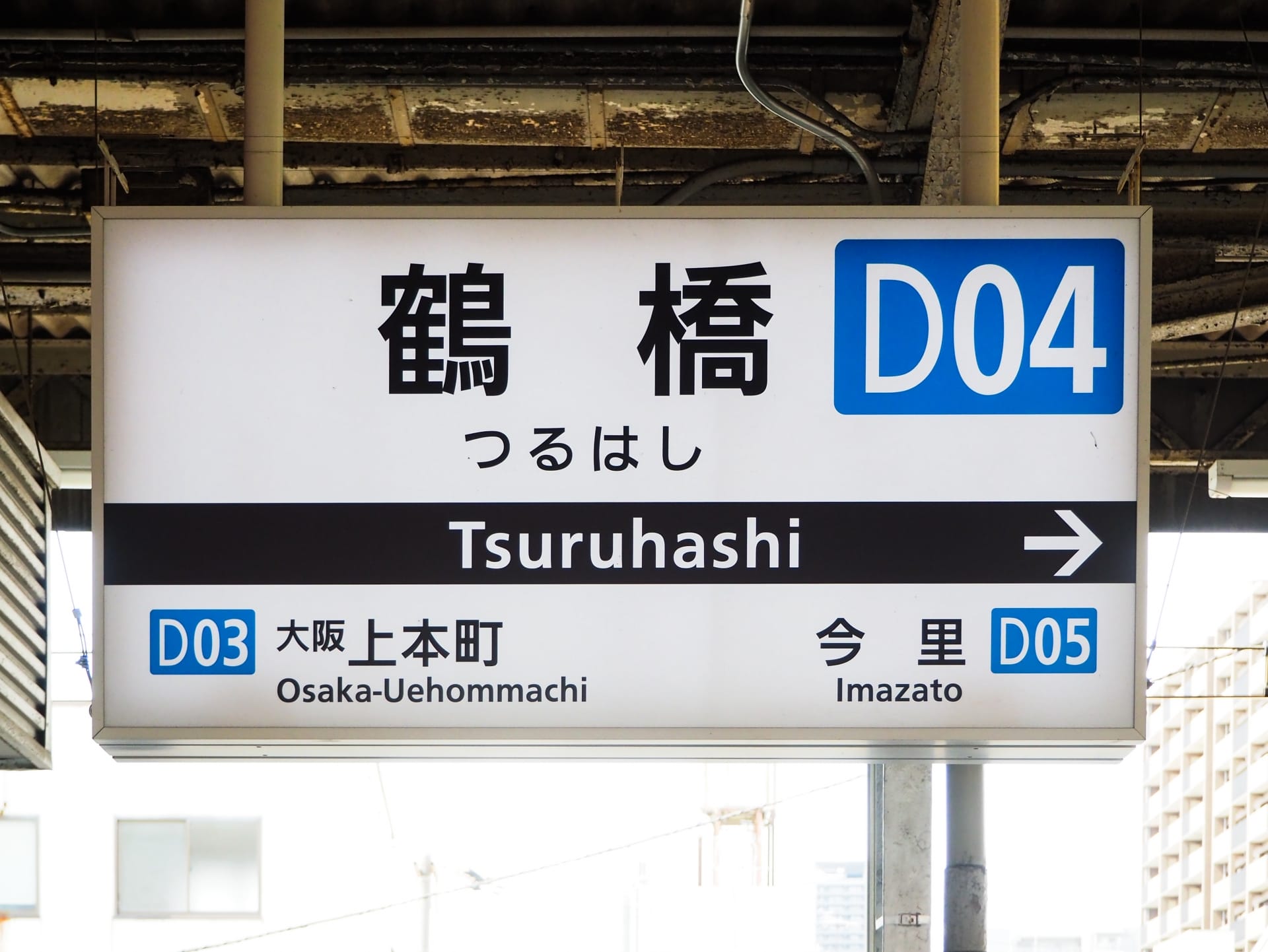 日本の鶴橋の駅標識は、D03 の大阪上本町と D05 の今里の間に位置する D04 への方向を示しています。近くには、個人に合わせた語学学習を提供する韓国語教室マンツーマンがあります。.