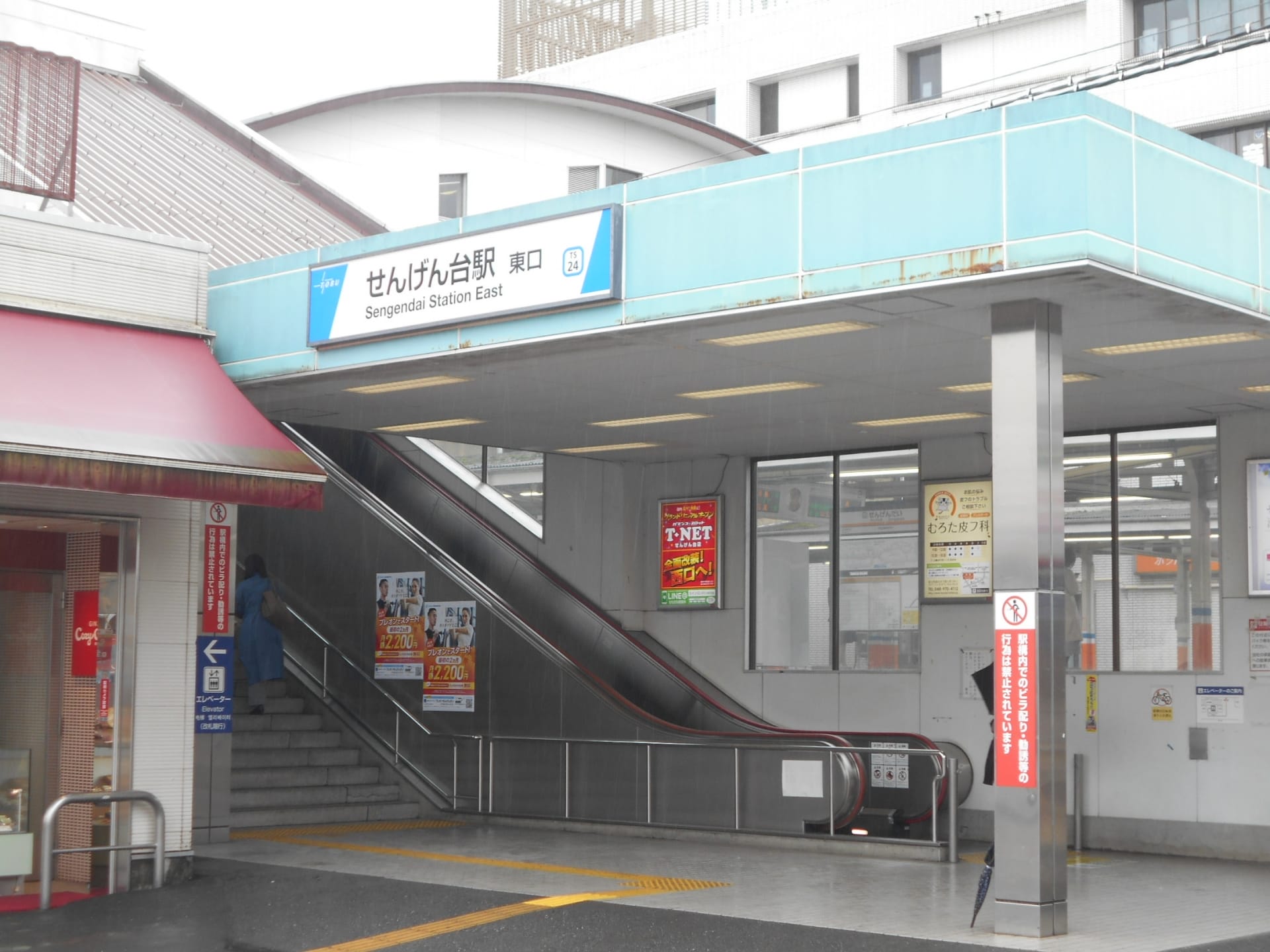 せんげん台駅東の入り口にはエスカレーターと階段があり、目に見える建物に囲まれた日本語の看板が設置されています。近くには、個人に合わせた語学学習を提供する韓国語教室マンツーマンがあります。.