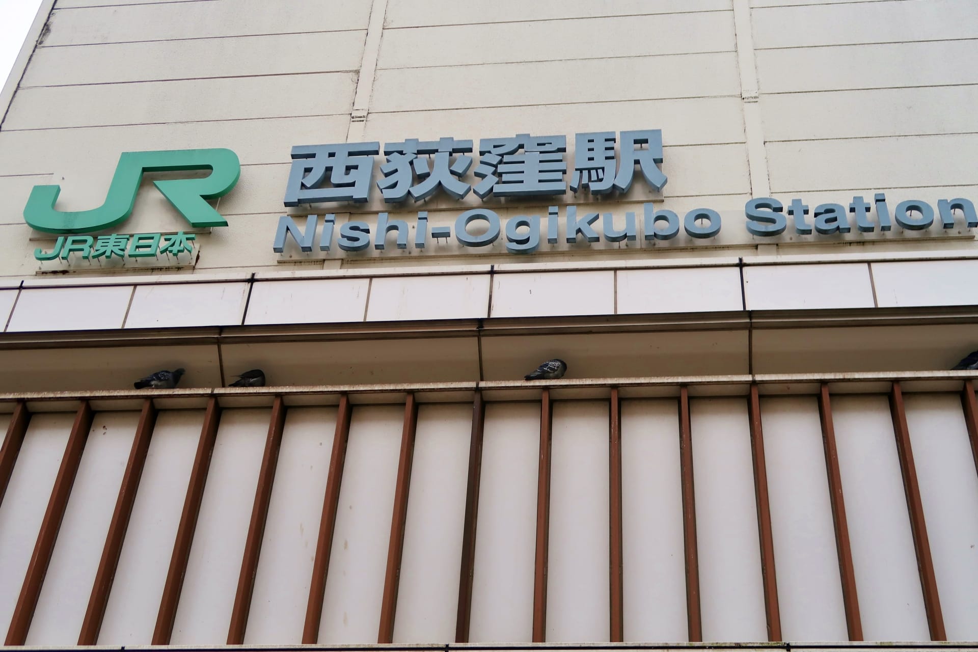 東京の西荻窪駅の標識。上に JR のロゴが付いています。標識の下の棚に鳩が止まっています。近くの韓国語教室マンツーマンは、西東京の活気ある西荻窪エリアで個人に合わせた学習体験を提供しています。.