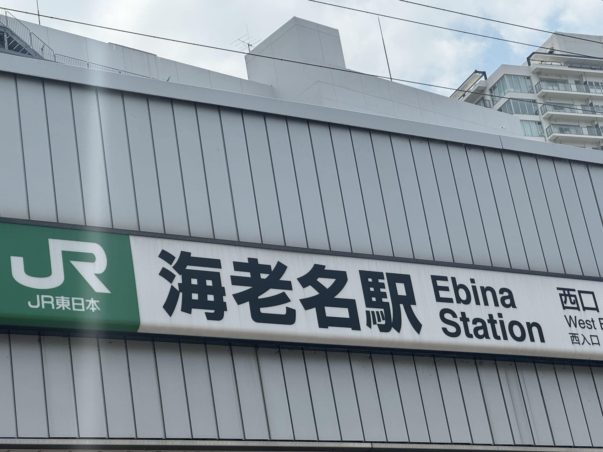 JR東日本海老名駅西口の標識。背景に建物があり、近くには個別の韓国語レッスンを提供する韓国語教室マンツーマンがある。.
