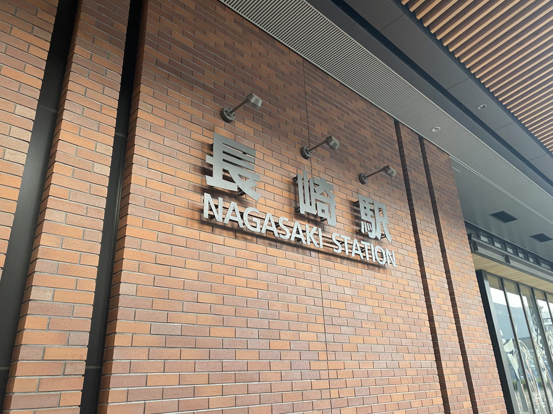 レンガの壁には、長崎の文字の横に、英語と日本語で「長崎駅」と書かれた標識が飾られている。.