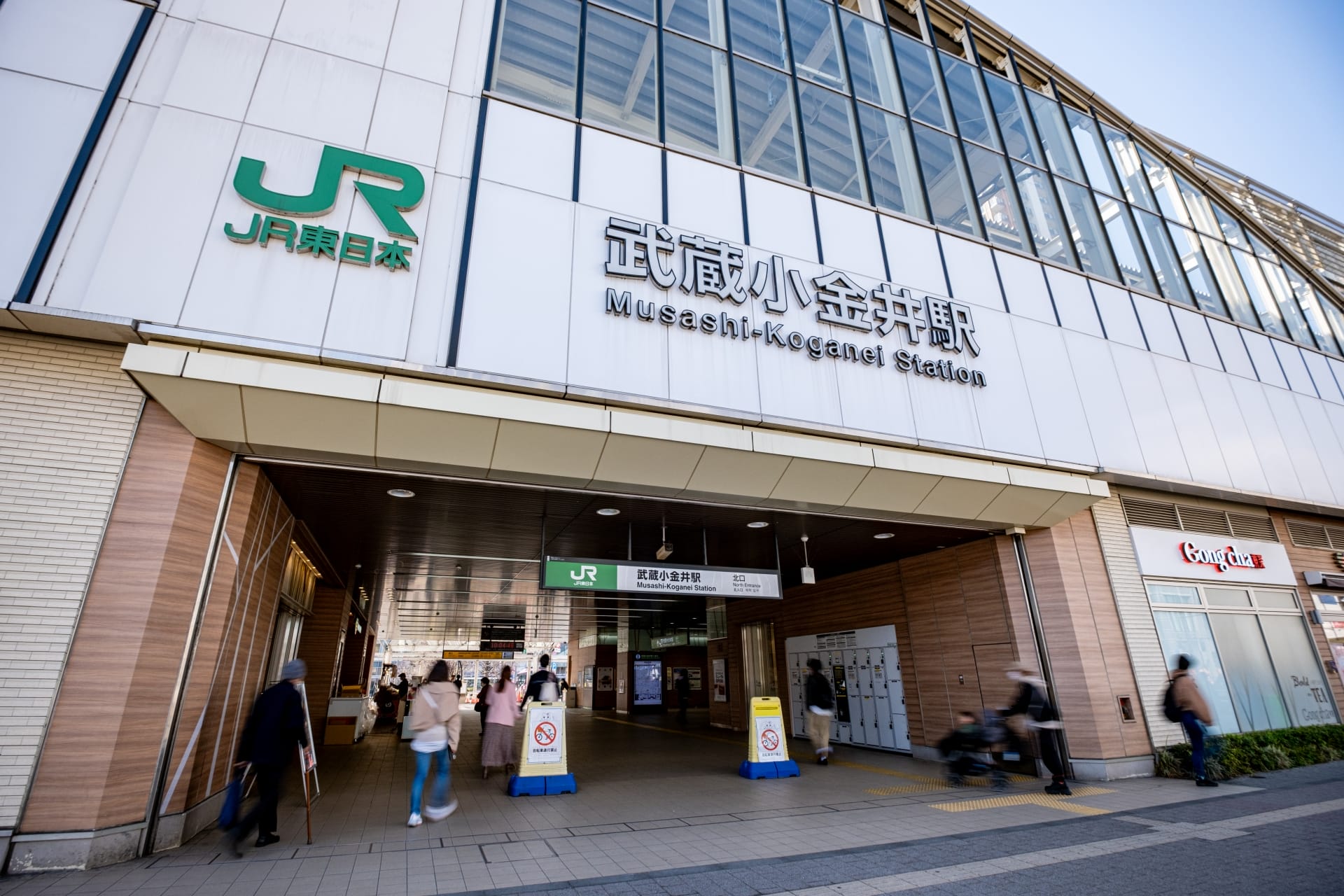 快晴の空の下、武蔵小金井駅の玄関口は行き交う人々で賑わっています。看板や部分的に見えるお店の中にある近くの韓国語教室マンツーマンでは、熱心な学習者向けに個別の言語レッスンを提供しています。.