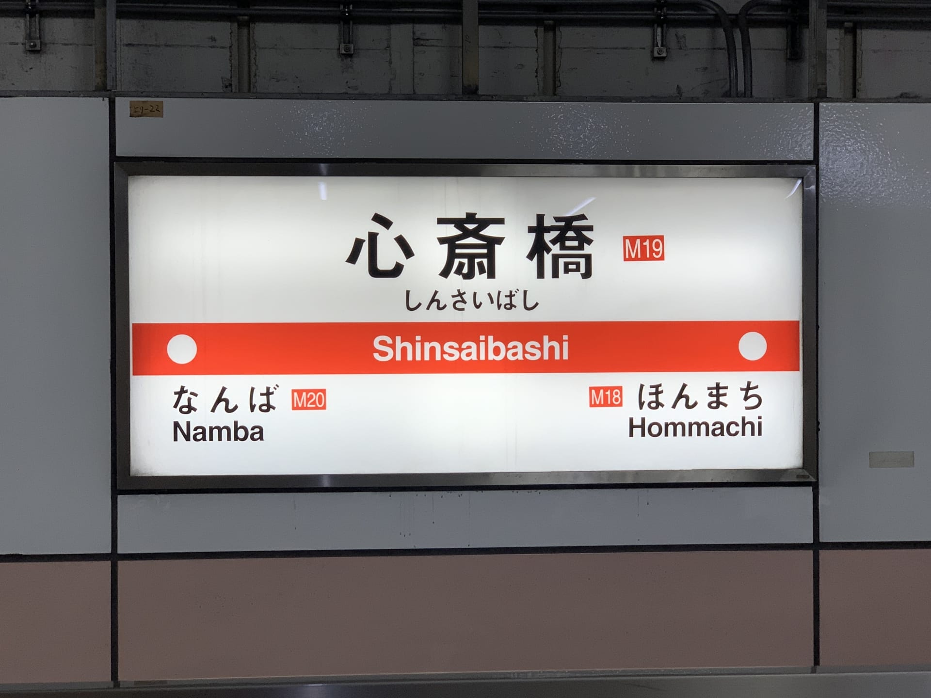 地下鉄の駅看板には「心斎橋」と「難波」（M20）と「本町」（M18）への行き方が日本語と英語で表示されており、地元の観光スポットや近くの韓国語教室マンツーマンなどの韓国語教室を探している旅行者に最適です。.