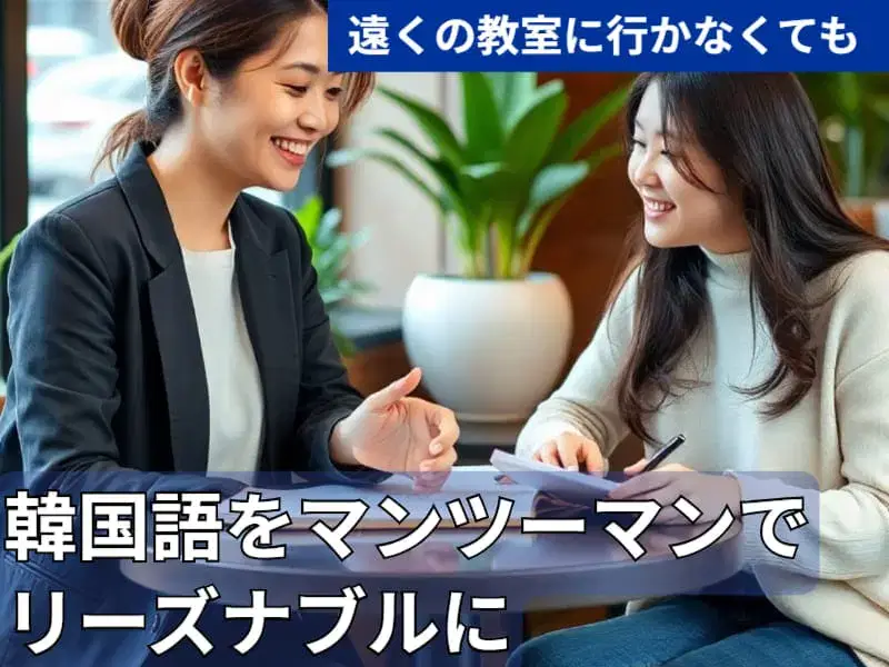 2人の女性がテーブルに座って微笑みながら話し、1人は紙とペンを持っている。.