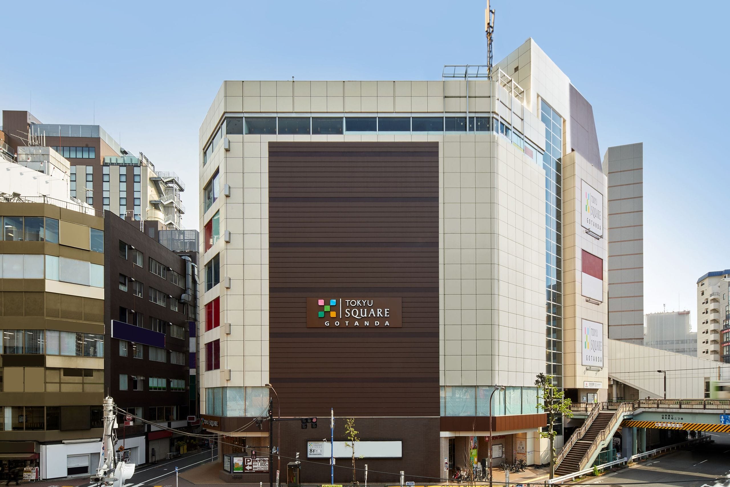 正面に「東急スクエア五反田」の看板を掲げた近代的で大きな雑居ビルがあり、その周りを他のビルが取り囲み、右手には歩道橋がある。.