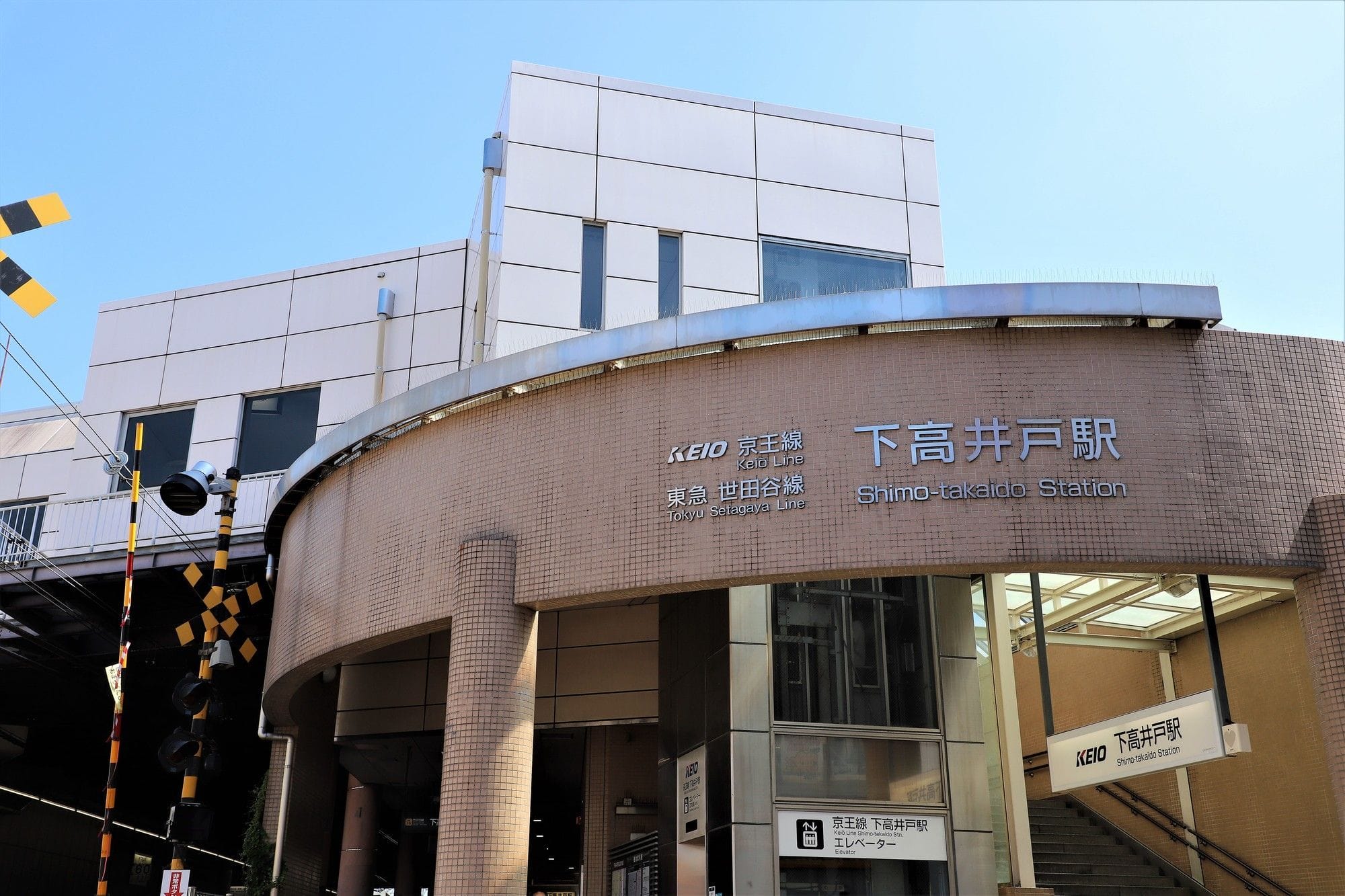 日本語と英語の標識、ベージュのタイル、階段、背景に近代的な建物のファサード。.