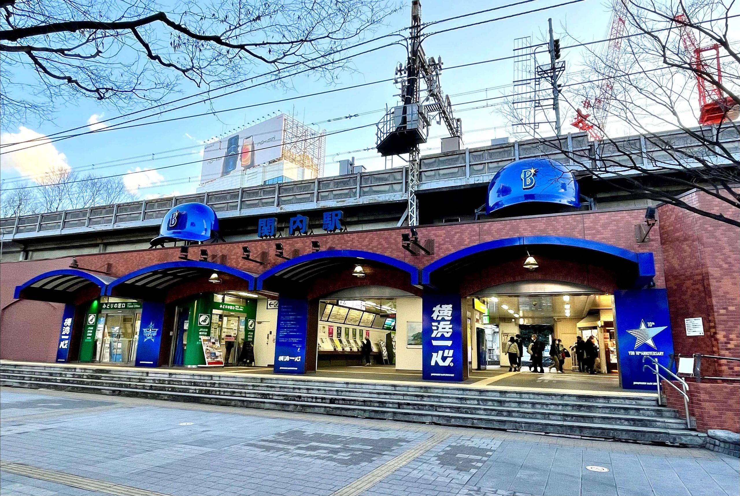 青いアーチ、券売機、歩く人々。アーチの上には大きな青いヘルメットが飾られている。.