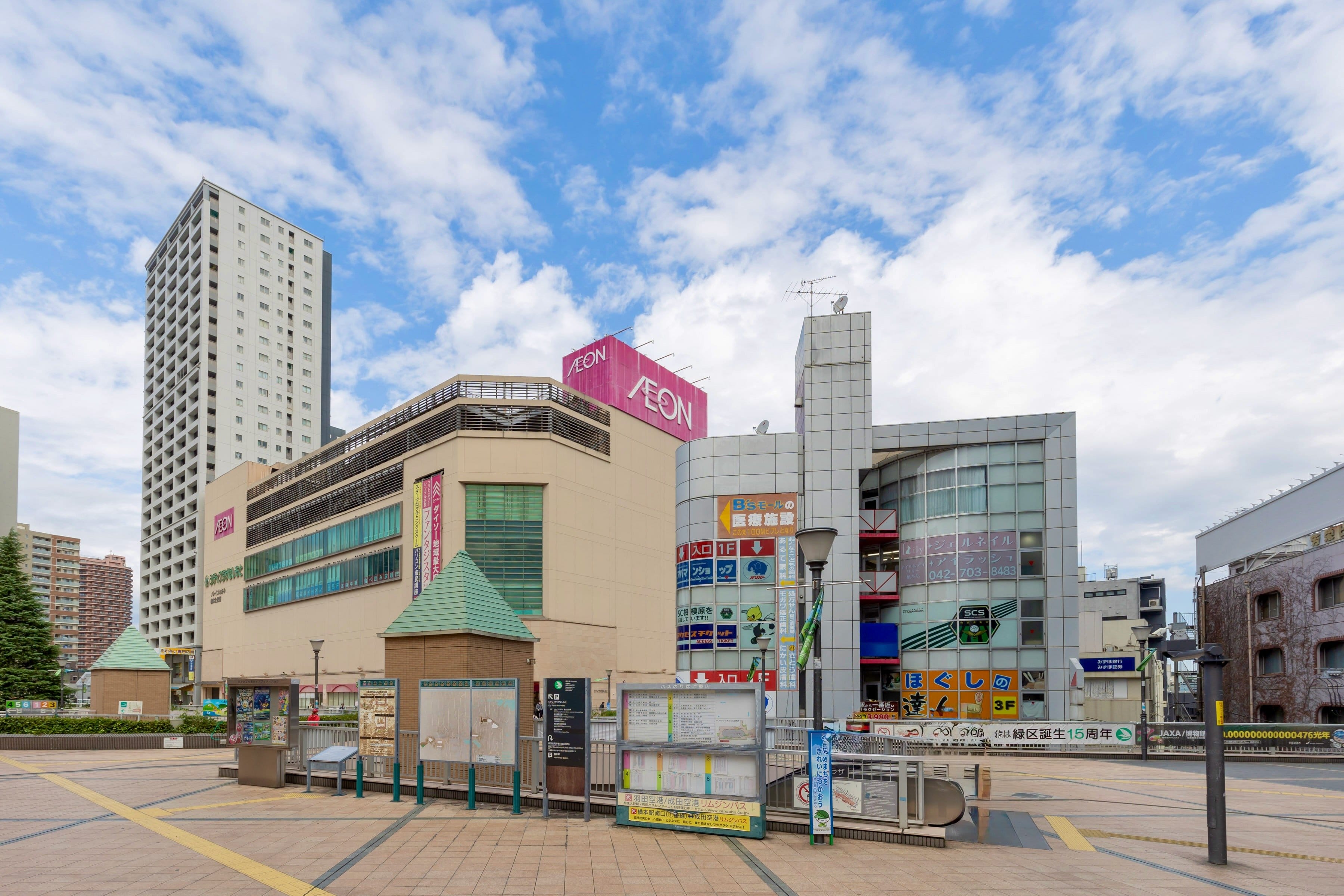 イオンの看板が掲げられた近代的なショッピング・コンプレックスは、高いビルと屋外掲示板に囲まれ、一部曇り空の下にある。.