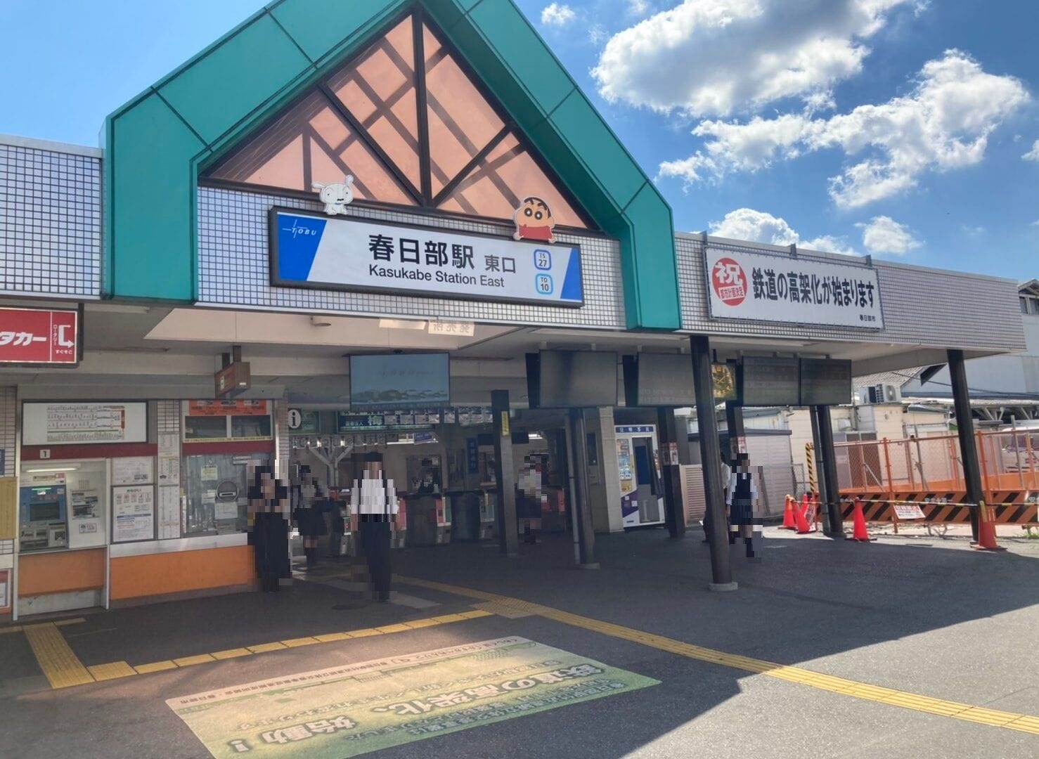 春日部駅東口。快晴の空の下、看板、券売機、出入りする人々。.