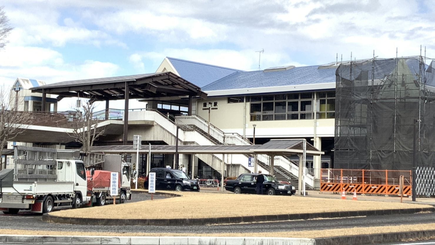 傾斜した青い屋根、外階段、駐車車両、右側に工事用の足場がある近代的な建物。.