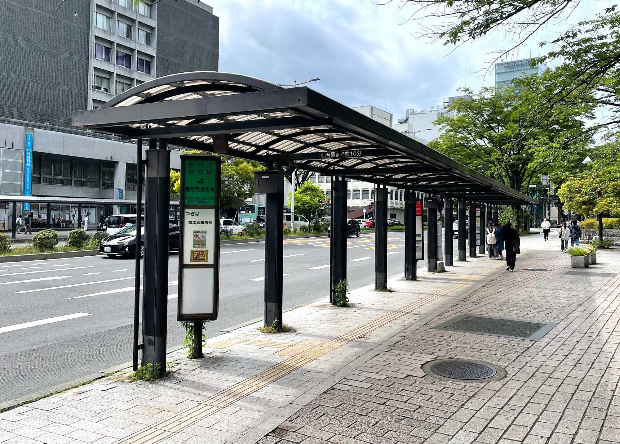 数車線の道路脇の歩道にあるデジタル表示の屋根付きバス停。.