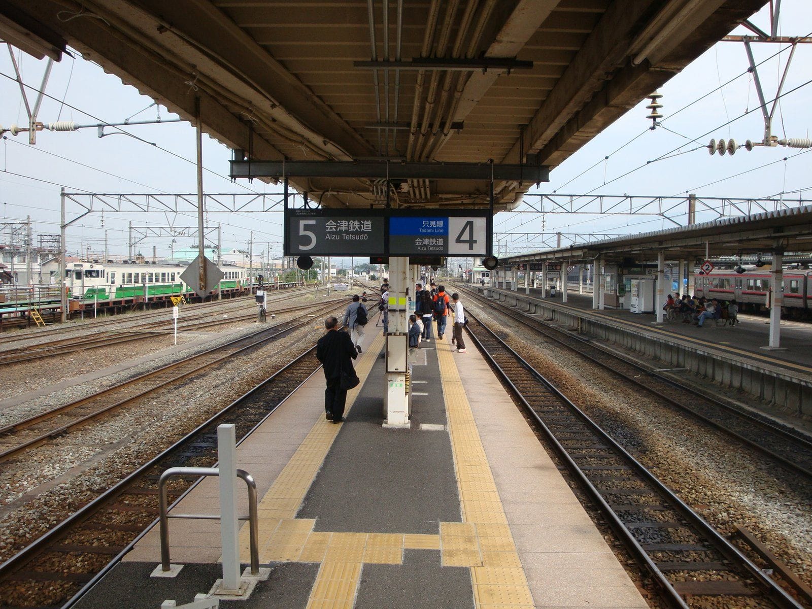 両側に線路が敷かれた駅のホームに立ち歩く人々。上の標識は4番と5番のホームを示す。.