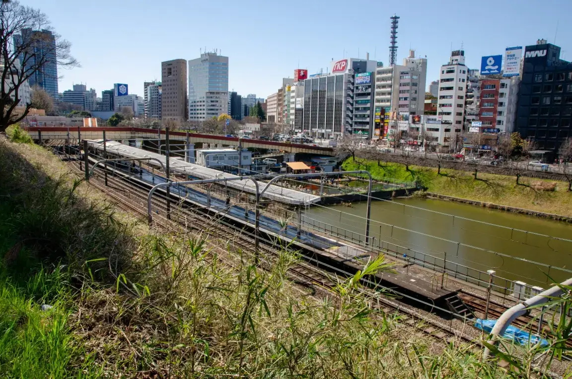 市谷の川沿いに広がる線路と駅を望む街並み。近代的なビル群に囲まれ、青空が広がるこのエリアの魅力を、口コミで探ってみたり、近くの韓国語教室に参加して体験してみてください。.