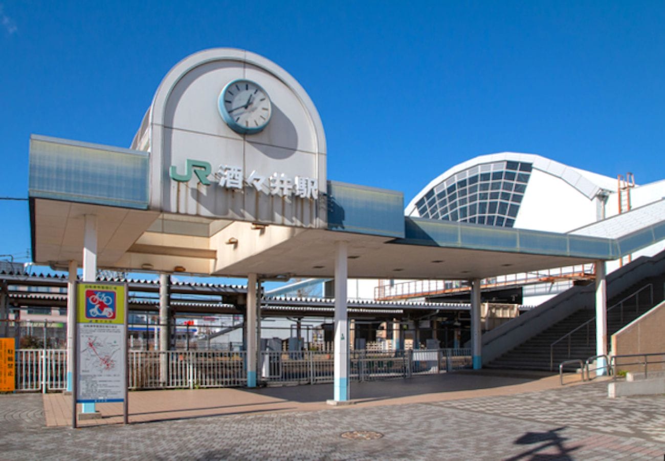 澄み切った青空の下、時計や階段、JRの看板がある駅の入り口。.