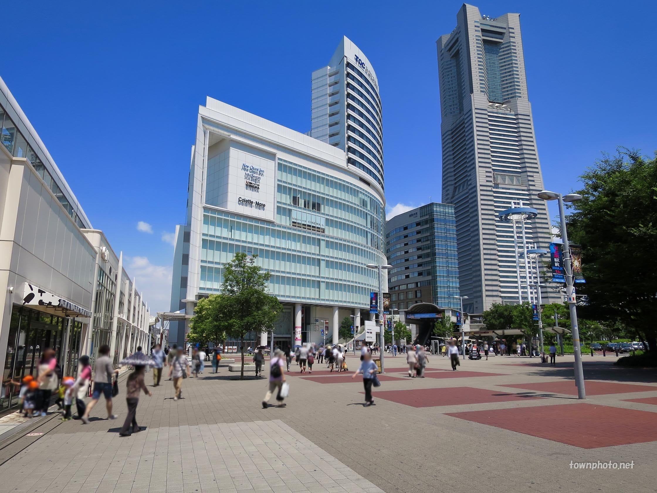高いオフィスビルが建ち並び、澄み切った青空が広がる近代的な都市広場を歩く人々。.